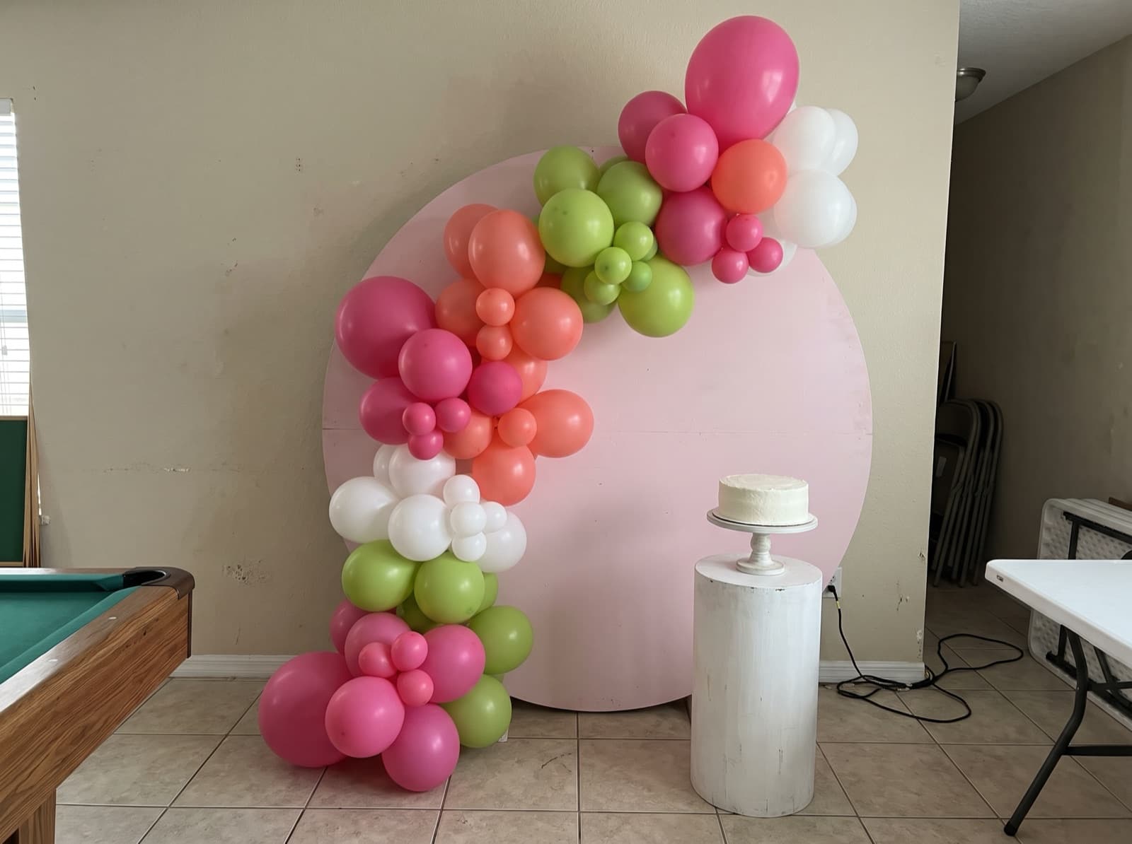 Round backdrop with a tropical organic balloon garland and a cake on a pedestal at an Orlando birthday party