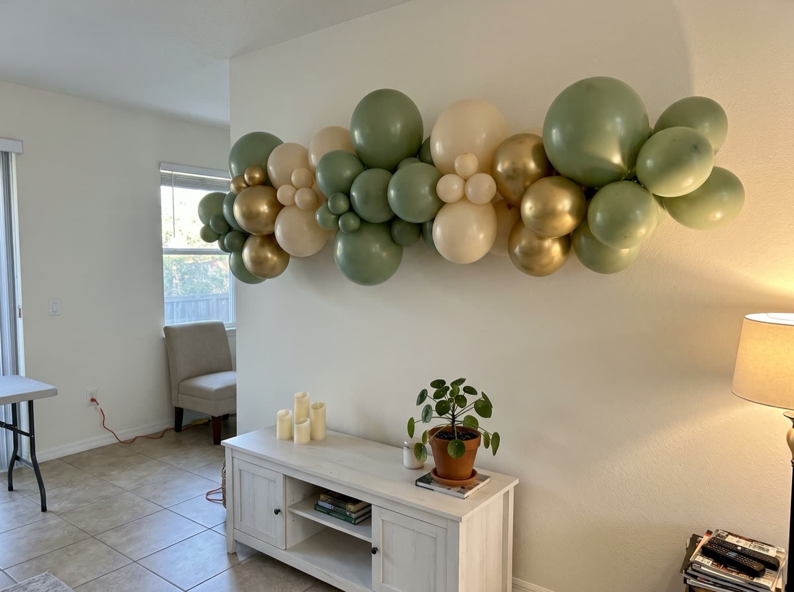 Organic balloon garland in sage, cream and gold above a TV console in an Orlando living room