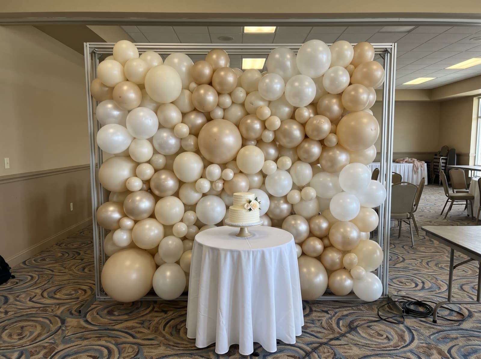 Organic balloon wall in ivory, pearl and champagne behind a cake table in an Orlando banquet hall